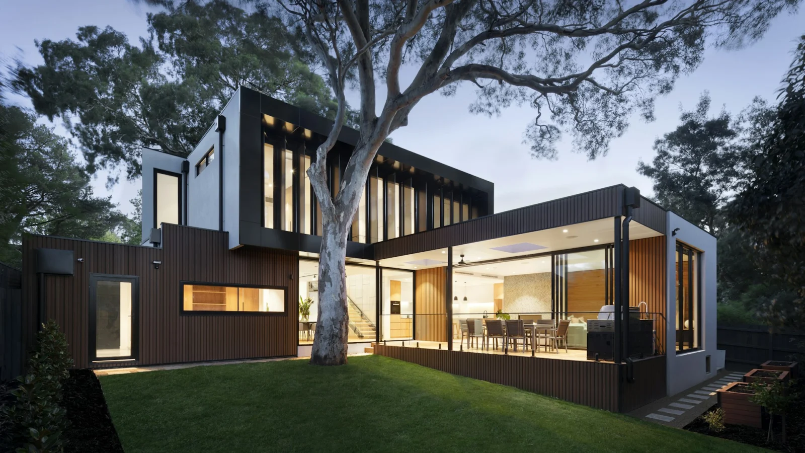 Contemporary house at dusk with warm light behind floor-to-ceiling glass