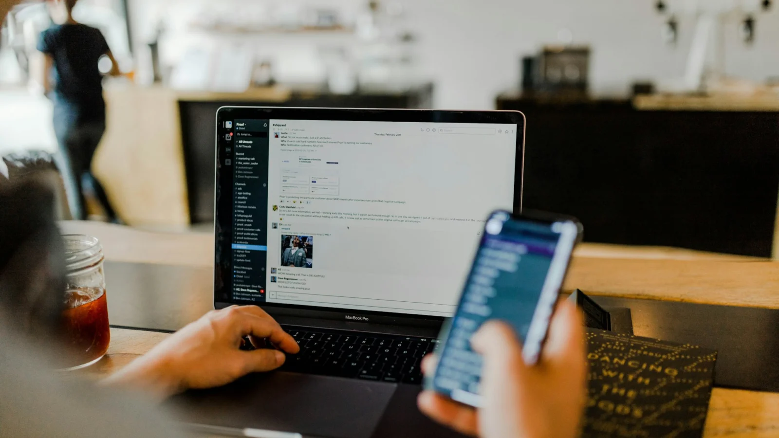 Person holding a smartphone next to a laptop
